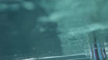 Su altı yansımalarında kamera ve bir kişi, renkli mayo giymiş genç bir kız suyun altında yüzmeye hazırlanıyor. Su altı kabarcıkları, yansımalar, turkuaz rengi ve yüksek kaliteli çekim.