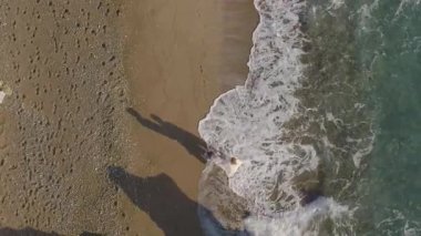 Dans eden, flört eden ve kıyı şeridinde kucaklaşan neşeli bir çiftin hava görüntüleri. Aşk, bağlantı ve eğlenceli kumsal anlarıyla dolu sinematik bir yaz aşkı.