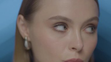 Büyüleyici mavi gözleri ve yumuşak makyajlı, sinematik ışıklandırma altında çeşitli yüz ifadelerini gösteren yüksek çözünürlüklü genç bir kadının yakın çekimi..
