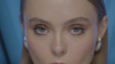 Açık tenli, mavi gözlü ve ince makyajlı yumuşak stüdyo ışıklarıyla yakalanmış genç bir kadının sinematik makro güzellik portresi. Değişen Işık ve Evrimleşen İfadesiyle Kadının Dinamik Yakın Çekimi