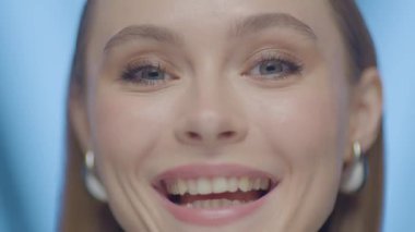 Güçlü ve odaklanmış bir ifadeye sahip, başını hafifçe eğmiş genç bir kadının yakın plan portresi. Yumuşak stüdyo ışıkları ve mavi arka plan altında yüksek çözünürlüklü görüntüler.