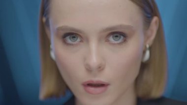 Güçlü ve odaklanmış bir ifadeye sahip, başını hafifçe eğmiş genç bir kadının yakın plan portresi. Yumuşak stüdyo ışıkları ve mavi arka plan altında yüksek çözünürlüklü görüntüler.