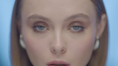 Büyüleyici mavi gözleri ve yumuşak makyajlı, sinematik ışıklandırma altında çeşitli yüz ifadelerini gösteren yüksek çözünürlüklü genç bir kadının yakın çekimi..