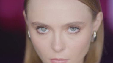 Renkli arka plan geçişleri ve stüdyo ışıklarıyla kameraya yoğun bir şekilde bakan genç bir kadının yakın çekimi. Zarif, minimal ve büyüleyici bir ifade..