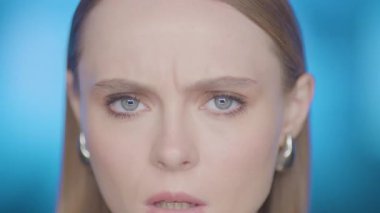 Renkli ışık altında kaşlarını çatan şüpheli bir kadının yakın çekimi. Şüphe ve endişeyi yansıtan etkileyici bir bakış.