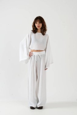 Şık, geniş kollu, geniş kollu, geniş paçalı pantolonlu, stüdyo modasında poz veren genç bir kadın..