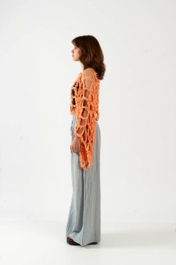 Profil görüntüsü: Turuncu örgü ören, siyah ve gri geniş pantolonlu genç bir kadın..