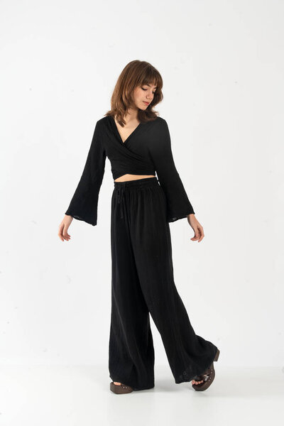 Элегантная женщина в черном топе с рукавами колокольчика и широкими штанами для ног, поза для ходьбы.