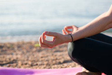 Deniz sahilinde yoga yapan, Lotus pozu veren, çıplak ayaklı, barışçıl spor yapan zinde bir kadın.