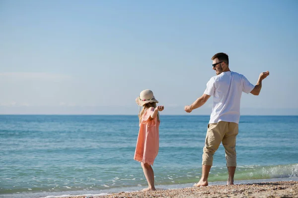 Father and daughter throw shells and stones in sea, beach summer vacation leisure family activity together