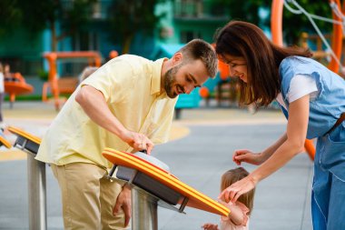 Ebeveynler ve yeni yürümeye başlayan kızlar oyun sahasında interaktif oyun oynuyorlar. Mutlu aile zamanları ve birlikte eğleniyorlar.