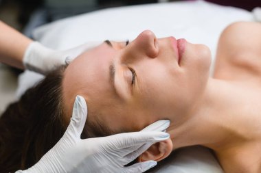 Beauty massage treatment to forehead skin, cosmetologist take care of woman face in professional salon