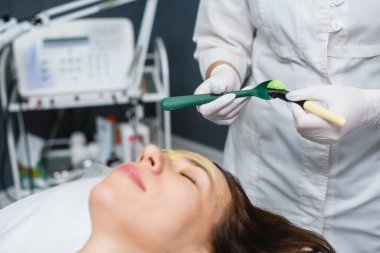 Cosmetologist prepare thick green skin care mask to apply on woman face at beauty salon, anti-aging treatment