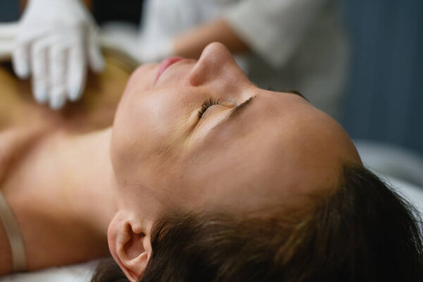 Женщина ложится в косметологический кабинет и готовится к процедуре электролиза, косметолог надевает крем в латексные перчатки на кожу