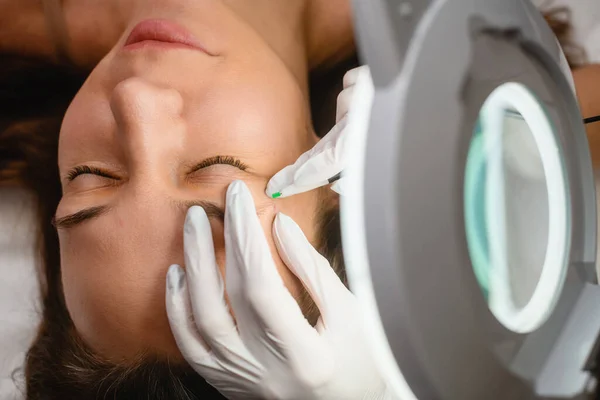 Female face under light in cosmetology clinic, relaxed woman laying during beauty facial skin procedures