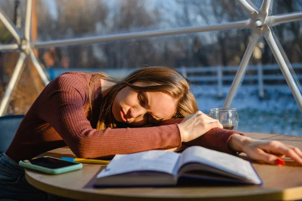 Tired young woman sleeps lying on the table with a notepad.