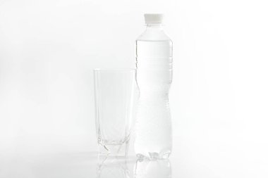 Boş bardak ve beyaz arka planda içme suyu olan plastik şişe.