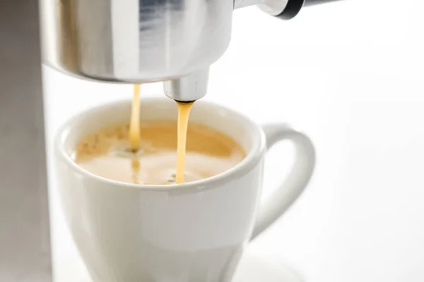 Espresso machine pouring strong fresh coffee into a ceramic cup, close-up.