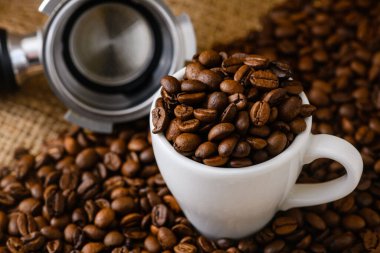 Kavrulmuş kahve çekirdekleri ve arka planda keçiboynuzu tutacağı. Tahta masa üzerinde, doğal doğal renklerde.