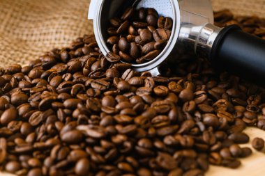 Kavrulmuş espresso kahve çekirdekleri ahşap masaya atılmış keçiboynuzu tutacağı ve malzeme arka planında içki.