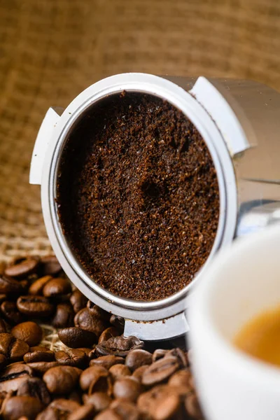 stock image Spent or used coffee grounds with portafilter and a cup of freshly brewed coffee in the background