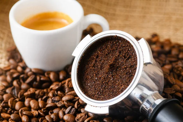 stock image Spent or used coffee grounds with portafilter and a cup of freshly brewed coffee in the background