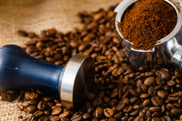 Coffee background with whole roasted beans, carob maker holder and tamper, professional barista tools