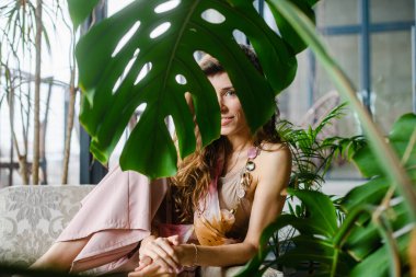 Bitkiler ve kadınlarla dolu doğal bir ev. Kocaman yeşil bir yaprak ve gülücük. Sıcak bir odada gün ışığı.