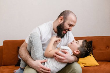 Baba küçük oğlana evde kucak açıyor duygusal yüzüyle, baba sevgisi ve aile içinde birlikte vakit geçiriyor.