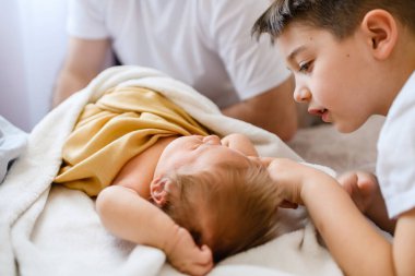 Ağabeyi yeni doğan bebeğe yatakta dokunur, tatlı bebeği battaniyenin altında mutlu bir aile, sevgi ve birliktelik ile gündüz vakti.