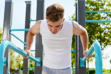 Genç bir atletik, spor sahasındaki dengesiz barlarda şınav çekiyor..