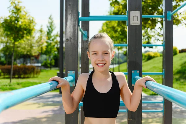 Portrait of a girl in sportswear near the horizontal bar and gymnastic bars outdoors. The concept of doing sports. Workout.