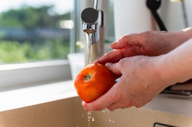 Woman washing fresh ripe tomatoes under tap water in kitchen, closeup