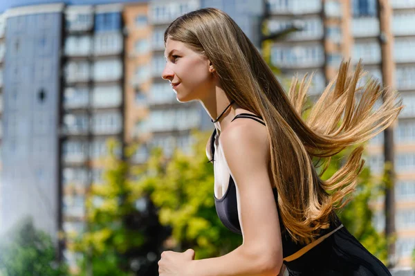 Young beautiful woman with long hair running outdoors at the city park. Long beautiful hair flutters in the wind. Side view. Profile of a running girl with long hair.
