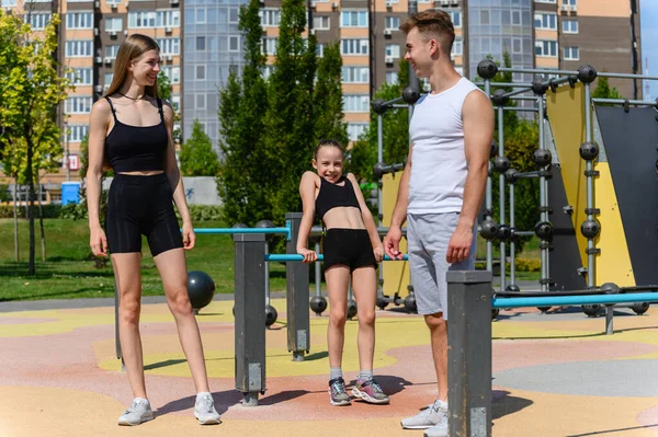 Young family on the sports ground doing exercises. Sports ground in the city park.