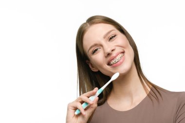 Kız elinde bir diş fırçası tutarak ve diş telleriyle güzel düz dişler göstererek geniş bir şekilde gülümsüyor..