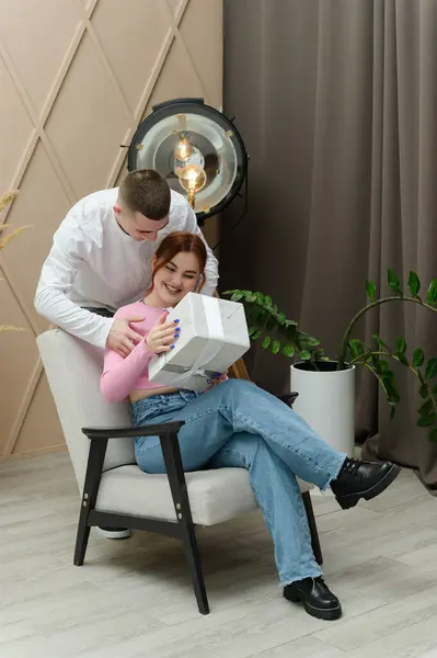 A man gives a gift to a girl. A man hugs a girl from behind. The girl is sitting in a chair.