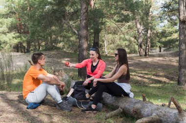 Yürüyüş sırasında düşmüş bir kütükte dinlenen üç arkadaş. Kız bir elma tutuyor. Yürüyüş sırasında bir mola..