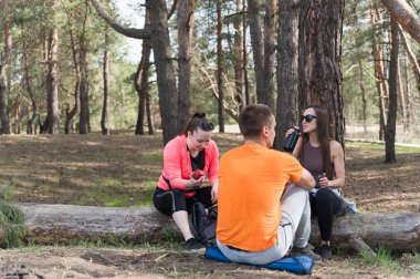 Yürüyüş sırasında düşmüş bir kütükte dinlenen üç arkadaş. Kız bir elma tutuyor. Yürüyüş sırasında bir mola..