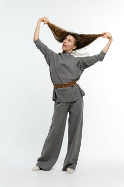 Uzun boylu esmer bir kadın, gülümsüyor ve beyaz arka planda saçlarıyla oynuyor. Pozitif duygular.