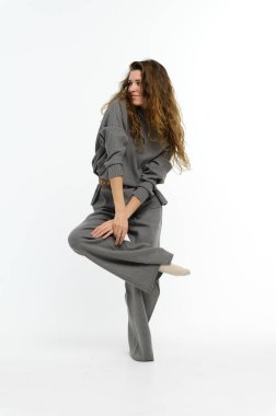 Genç bir kadın tek bacakla dengede durur. Kız beyaz arka planda dans ediyor..