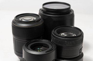 Beyaz yüzeye yakın düzenlenmiş dört siyah kamera lensi, insan yok, üst görüş, görünür cam detayları, minimal arka plan, yumuşak ışıklandırma, modern fotoğraf ekipmanları.