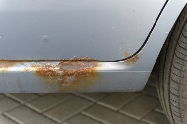 Pas ve aşınmaya uğramış, pul pul pul ve oksitlenmiş metali asfaltlanmış bir yüzeyde yakalayan bir arabanın yakın çekim görüntüsü..