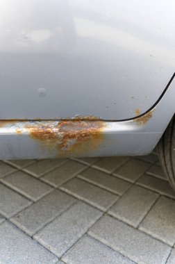 Pas ve aşınmaya uğramış, pul pul pul ve oksitlenmiş metali asfaltlanmış bir yüzeyde yakalayan bir arabanın yakın çekim görüntüsü..
