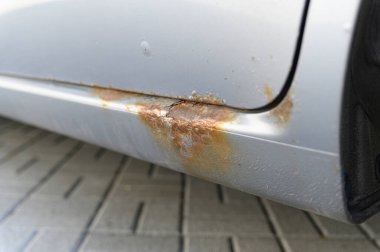 Pas ve aşınmaya uğramış, pul pul pul ve oksitlenmiş metali asfaltlanmış bir yüzeyde yakalayan bir arabanın yakın çekim görüntüsü..