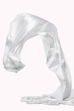 Hareket halindeki yumuşak beyaz kumaşın soyut görüntüsü, temiz beyaz bir zemine doğru havada uçuyor ve kıvrılıyor. Stüdyo ışıklandırması, izole, insan yok..