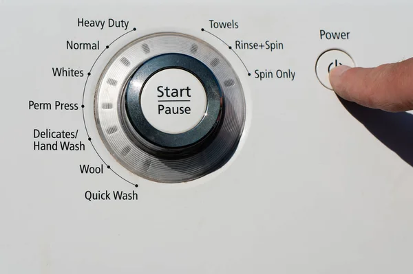 A person pressing the power button on a washing machine. High quality photo