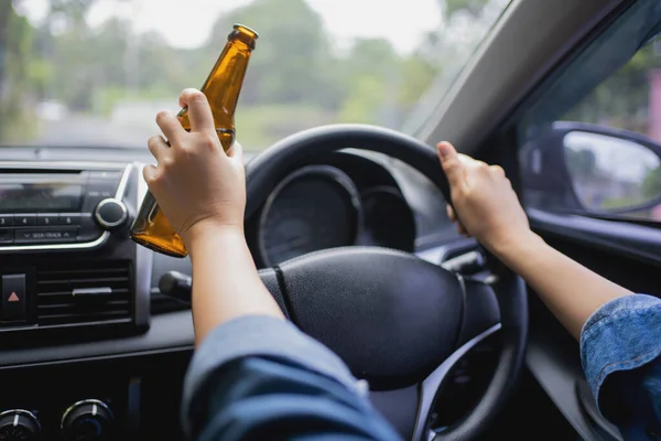 Woman is drinking a bottle of beer while driving a car. Breaking the law and drinking alcohol while driving