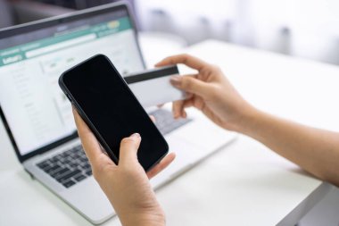 Akıllı telefon kullanan genç bir kadının elinde beyaz ekranı gösterirken diğer elinde kredi kartı olacak ve masanın yanına defter koyulacak..