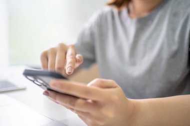 İş yerinde mobil cihazlar kullanırken dizüstü bilgisayarın üzerindeki akıllı telefon ekranını gösteren genç kadının elleri